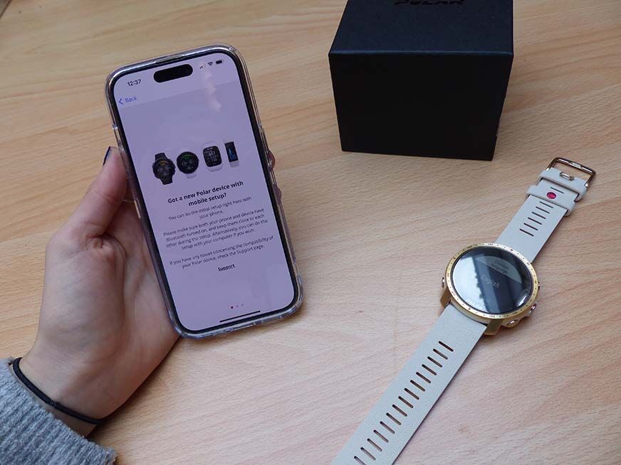 Man sieht die Polar Grit X Pro neben einem iPhone. 